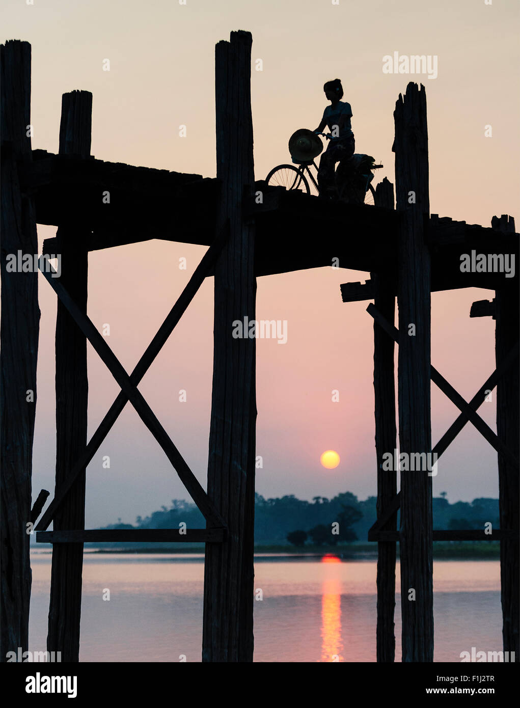 Silhouette d'une femme birmane à bicyclette Équitation sur U Bein Bridge au coucher du soleil. Banque D'Images