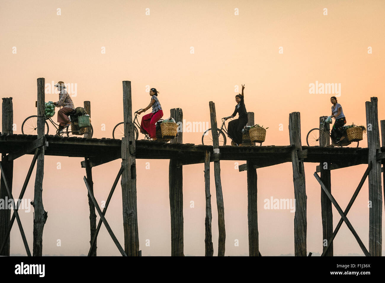 Clignote en signe de paix birmane sur un vélo sur U Bein Bridge au coucher du soleil. Pont U Bein Birmanie, Myanmar Banque D'Images