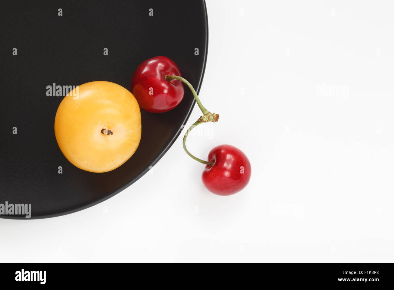 Prune jaune et rouge cerises sur la plaque noire Banque D'Images