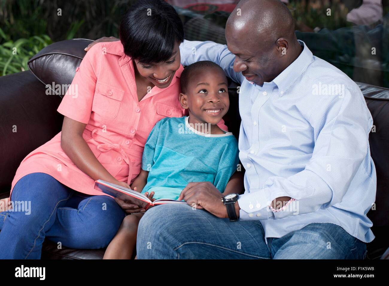 Les jeunes parents africains la lecture à leurs fils sur un canapé Banque D'Images