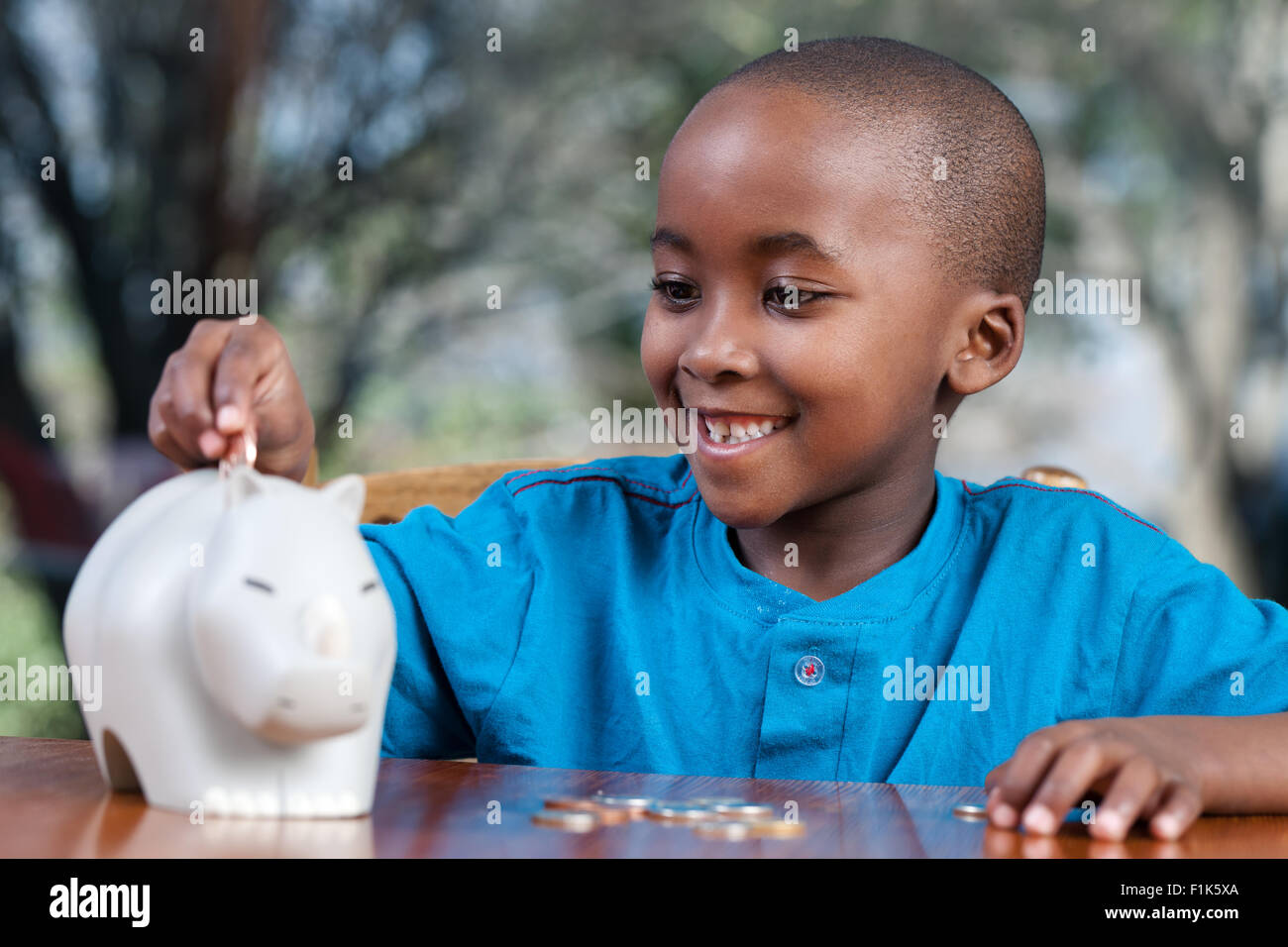 Jeune garçon africain mettre des pièces dans une tirelire en souriant Banque D'Images