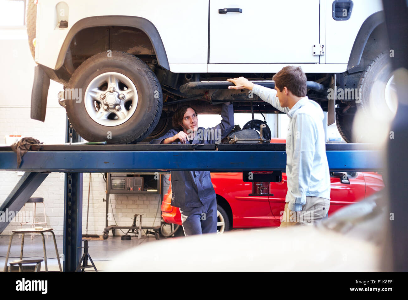 Voiture de mécanicien sous parler à client en atelier de réparation automobile Banque D'Images
