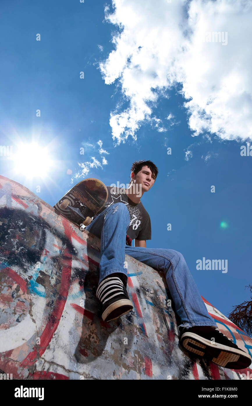 Adolescent est assis sur une rampe de halpipe avec une planche à roulettes Banque D'Images