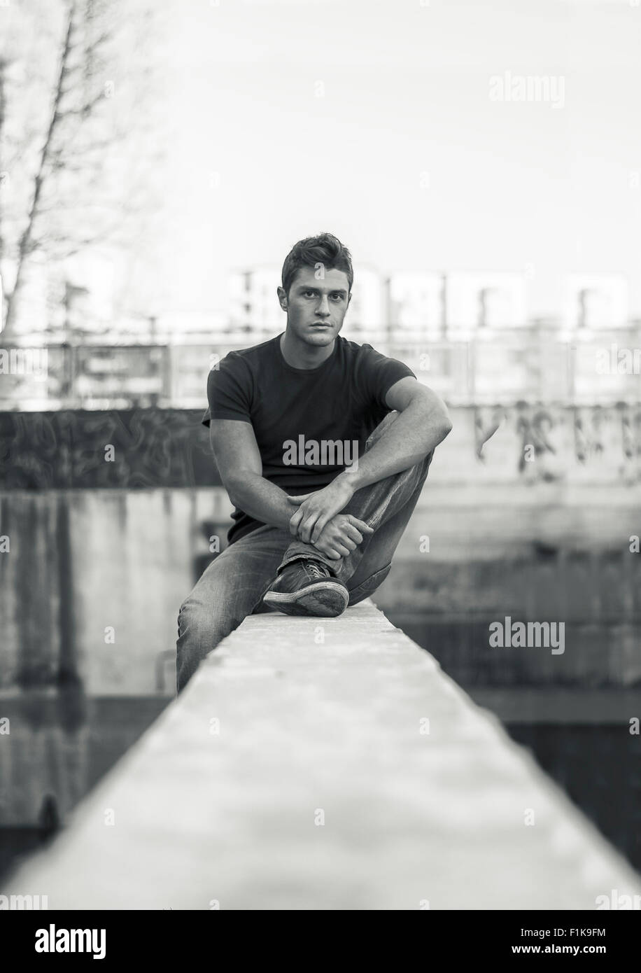 Young attractive man sitting on sale wall, looking at camera, de l'environnement urbain Banque D'Images