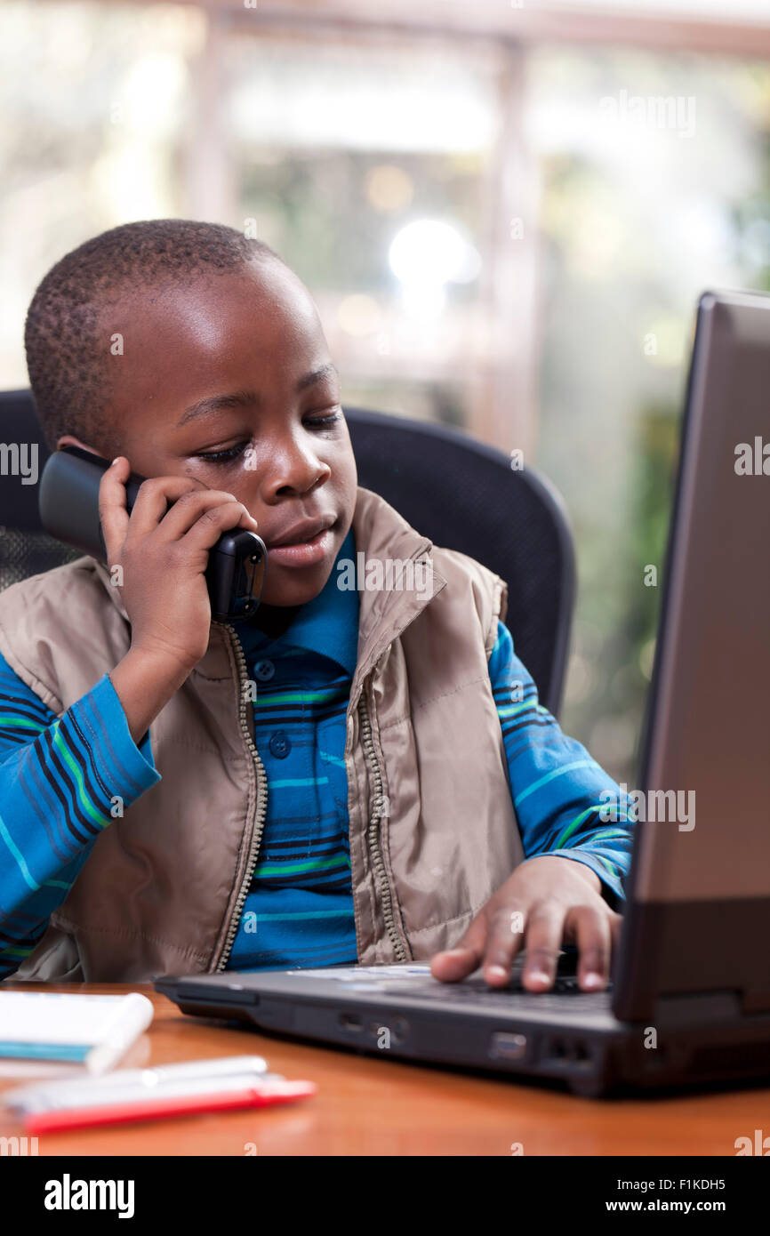 Jeune garçon africain assis à son père 24, jouant sur l'ordinateur portable et de parler au téléphone Banque D'Images