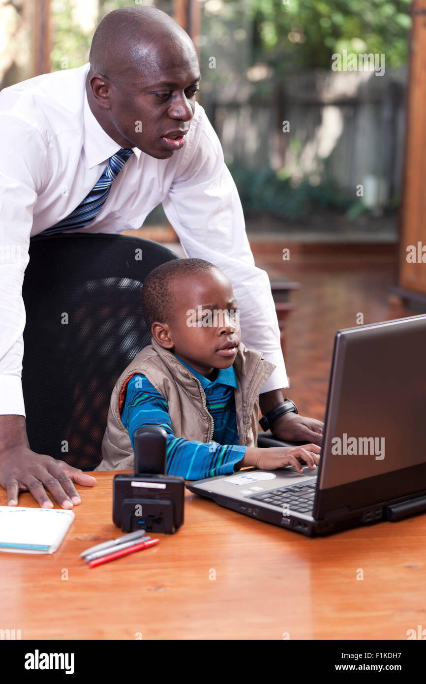 Un jeune garçon est assis de l'Afrique chez son père 24, jouant sur un leptop tandis que son père veille sur son épaule Banque D'Images