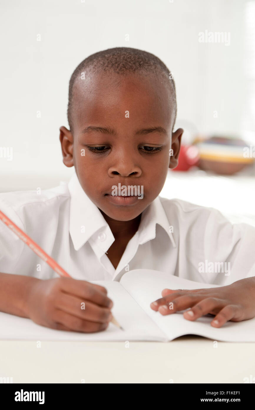 Jeune garçon africain fait ses devoirs dans la cuisine Banque D'Images