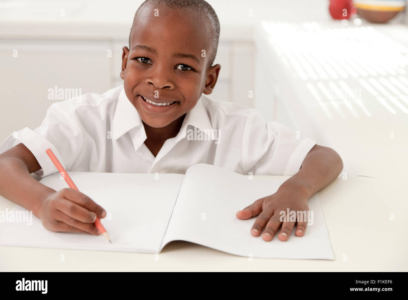 Jeune garçon africain fait ses devoirs dans la cuisine, smiling at camera Banque D'Images
