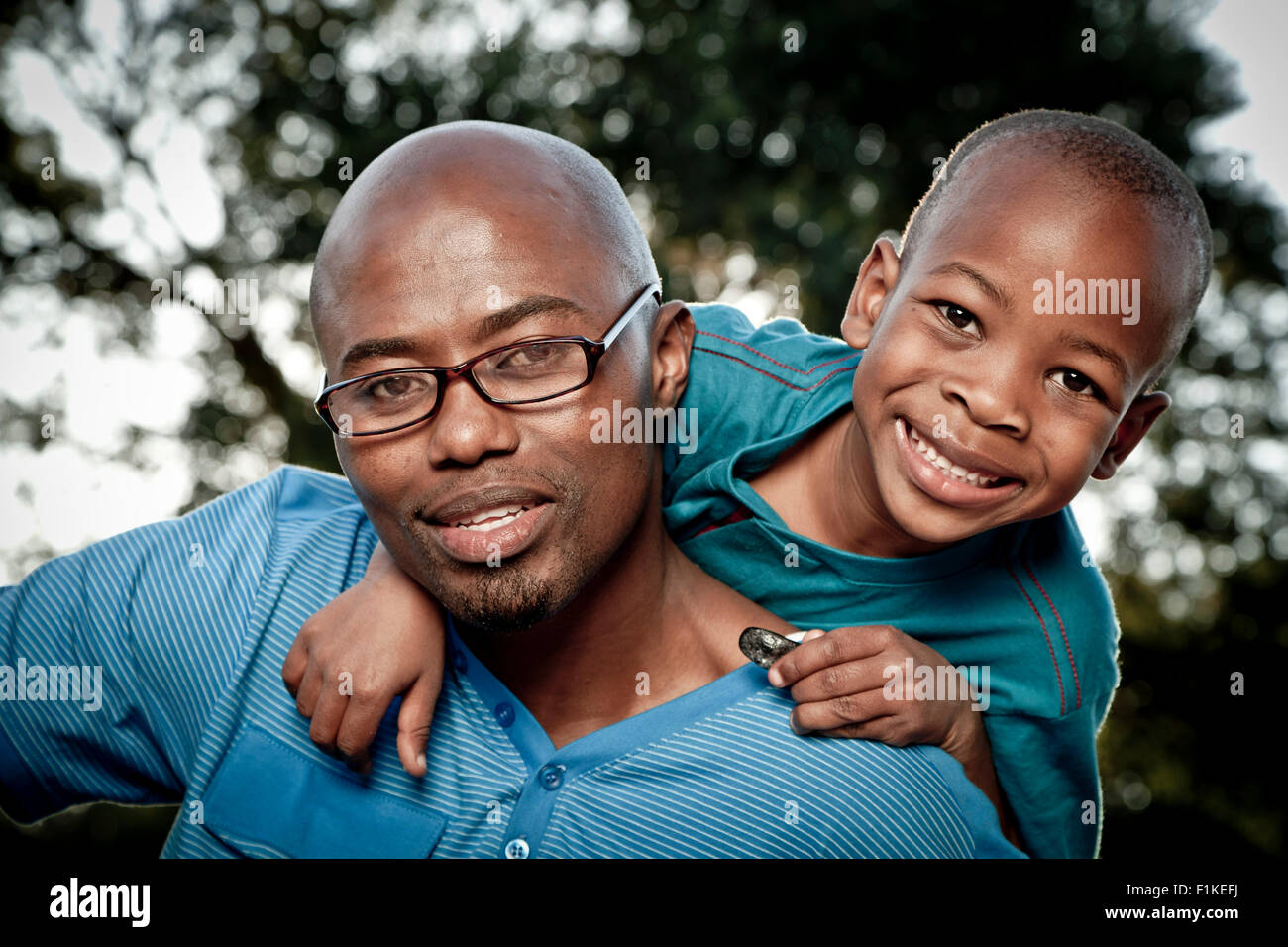 Jeune garçon africain et son père s'asseoir dans un parc, smiling at camera Banque D'Images