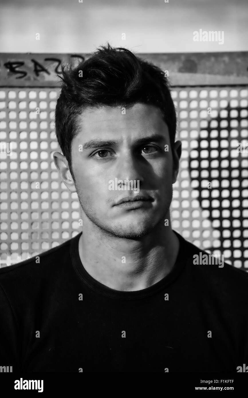 Portrait of attractive young man looking at camera, contre fond de grille, tourné en noir et blanc Banque D'Images