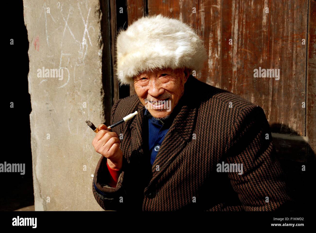 Pengzhou, Chine Chinois : Un homme portant un chapeau de fourrure et fumer une cigarette dans un porte-assis Banque D'Images