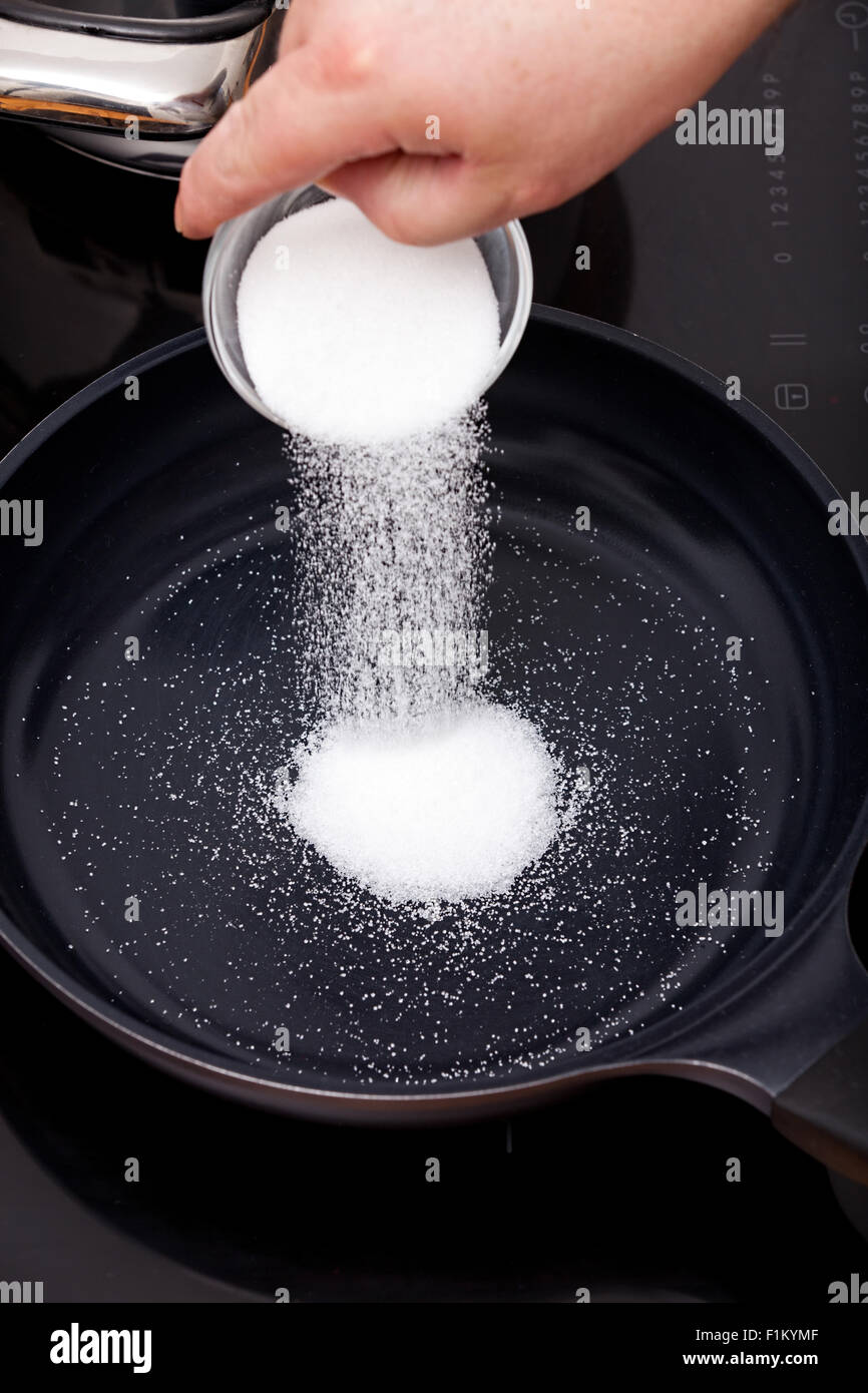 Versez le sucre dans un bol en verre dans une poêle pour caraméliser Banque D'Images
