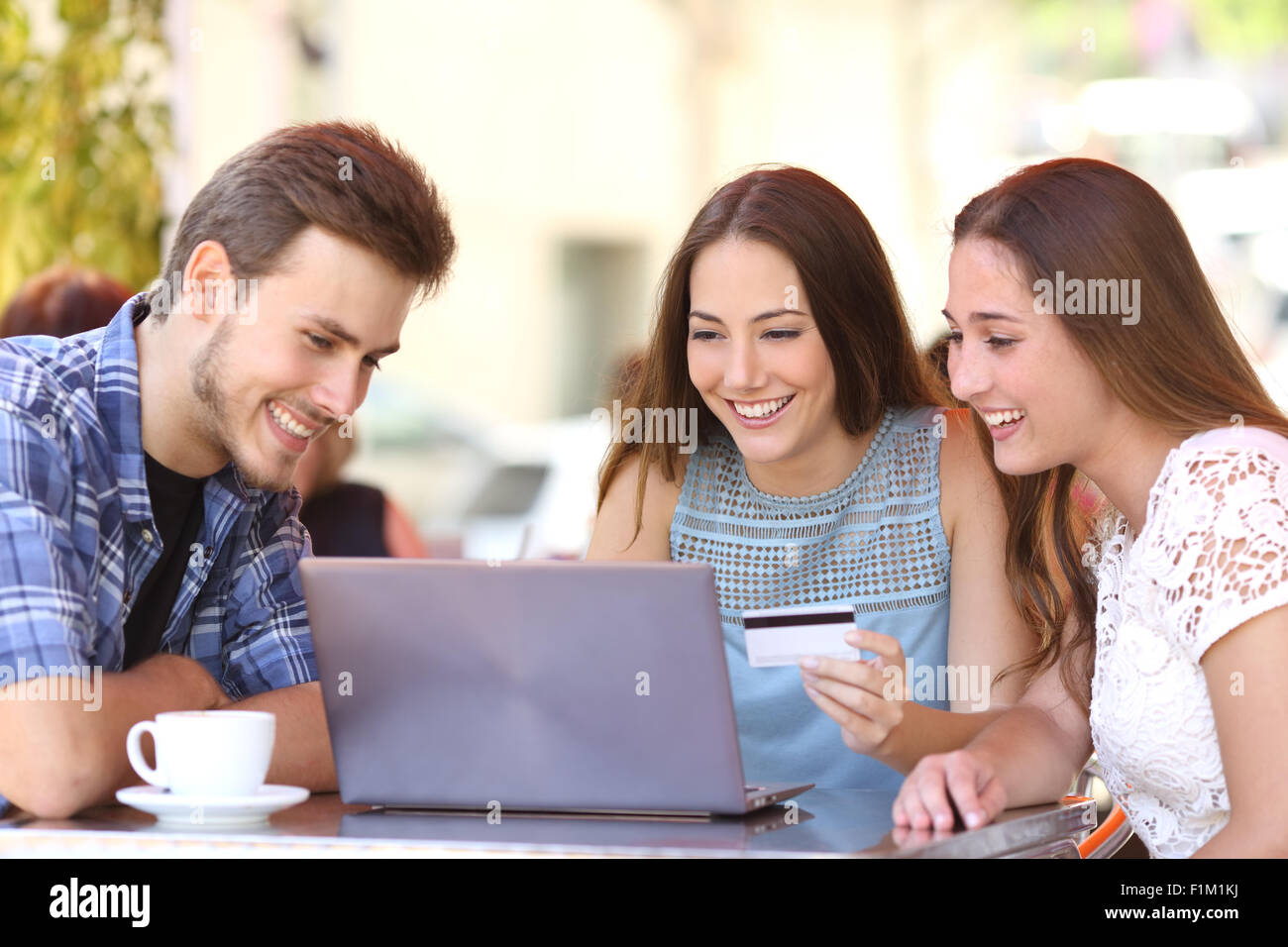 Trois amis heureux magasinage en ligne avec une carte de crédit et d'un ordinateur portable dans un café Banque D'Images