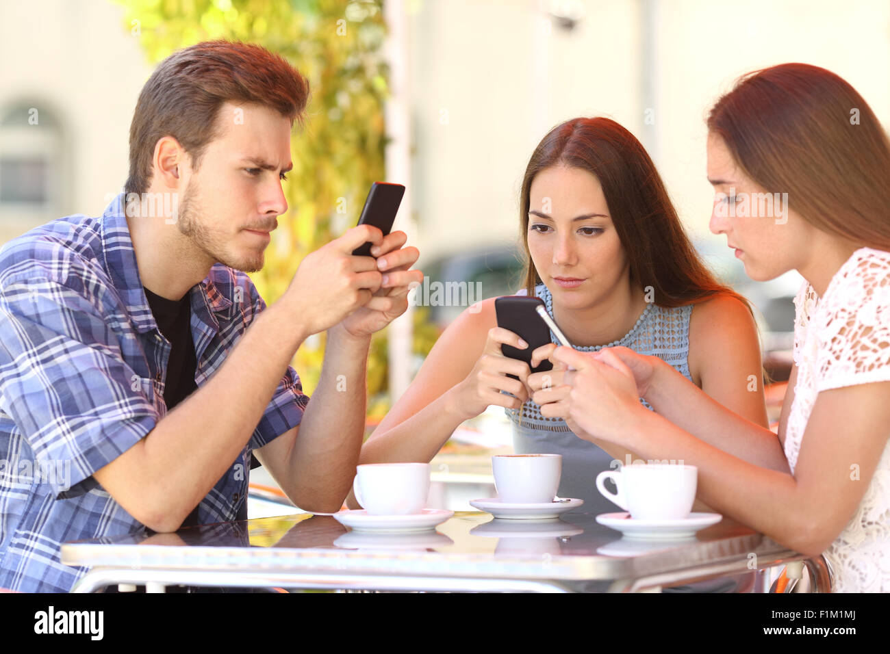 Groupe de trois amis toxicomanes smart phone dans un café terrasse tout le monde avec un téléphone cellulaire Banque D'Images