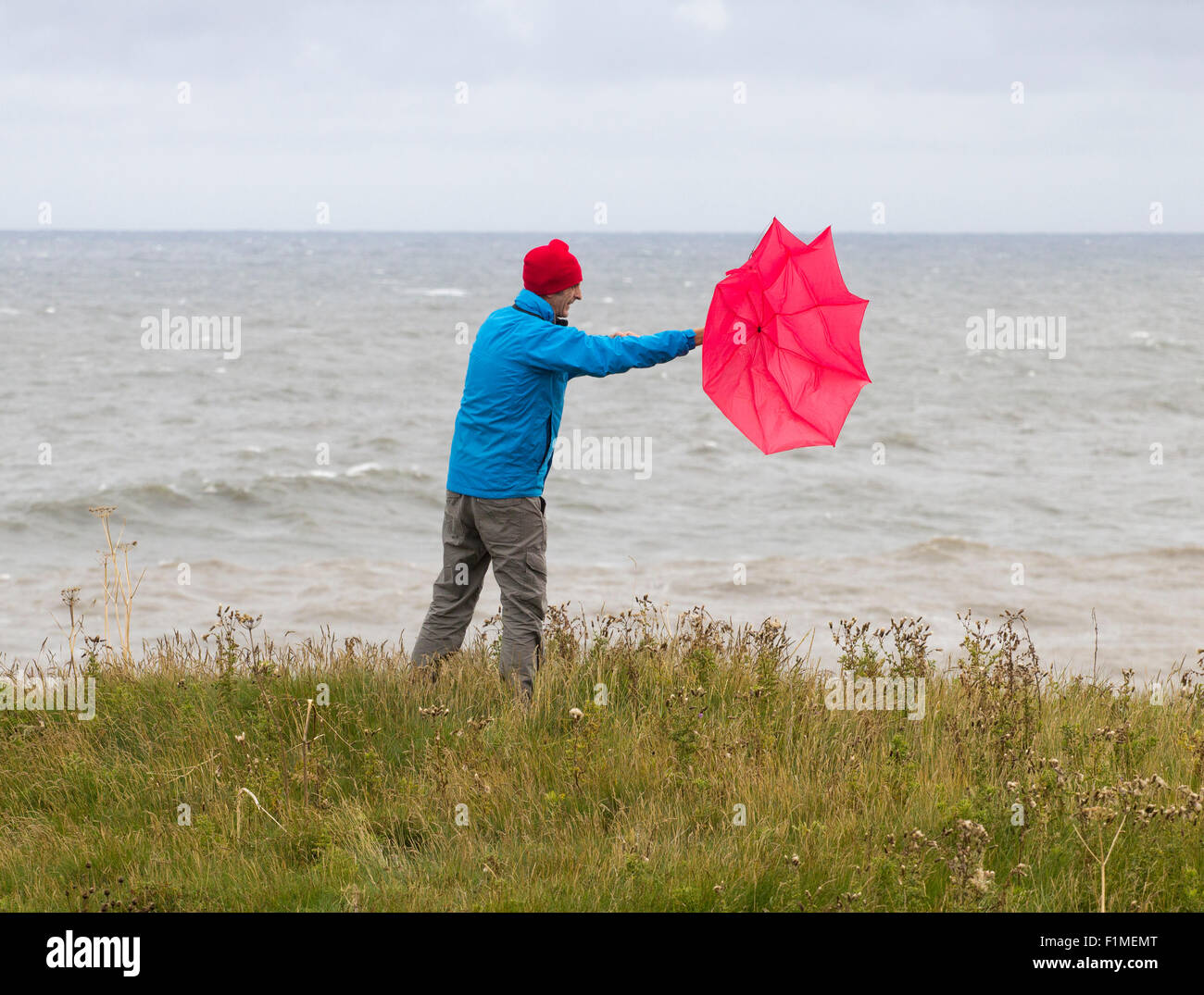 Homme avec un parapluie rouge le jour du vent/de l'orage. ROYAUME-UNI Banque D'Images