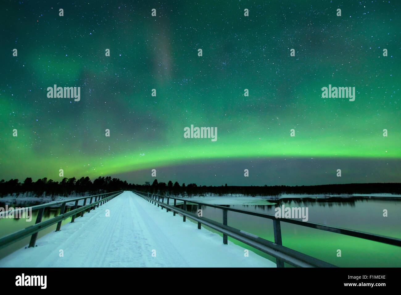 Des aurores boréales) sur un pont et une rivière dans un paysage d'hiver enneigé en Laponie finlandaise. Banque D'Images
