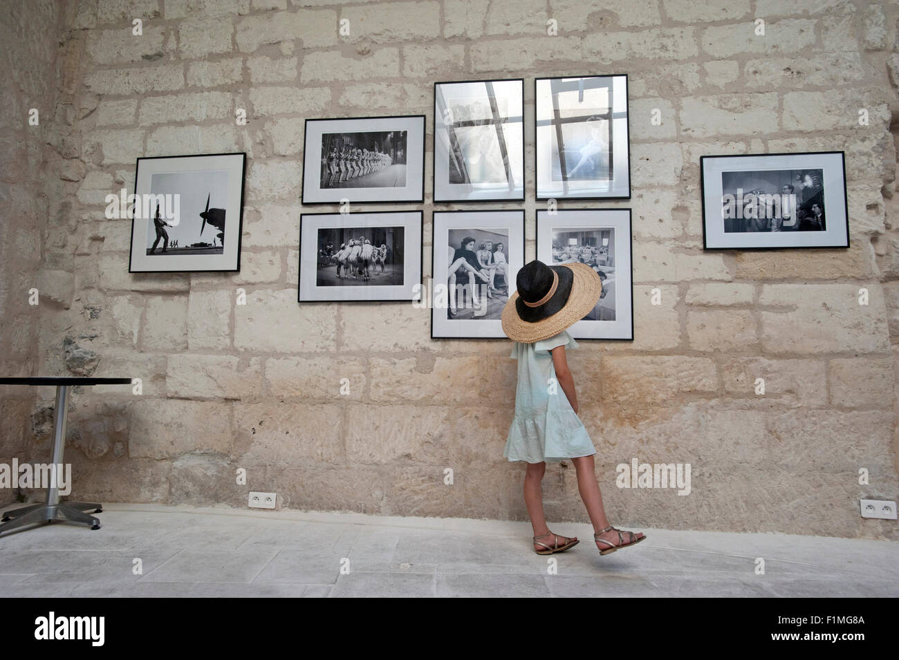 Une petite fille porter deux chapeaux porte sur des photographies anciennes dans une galerie d'art à Arles, France. Banque D'Images