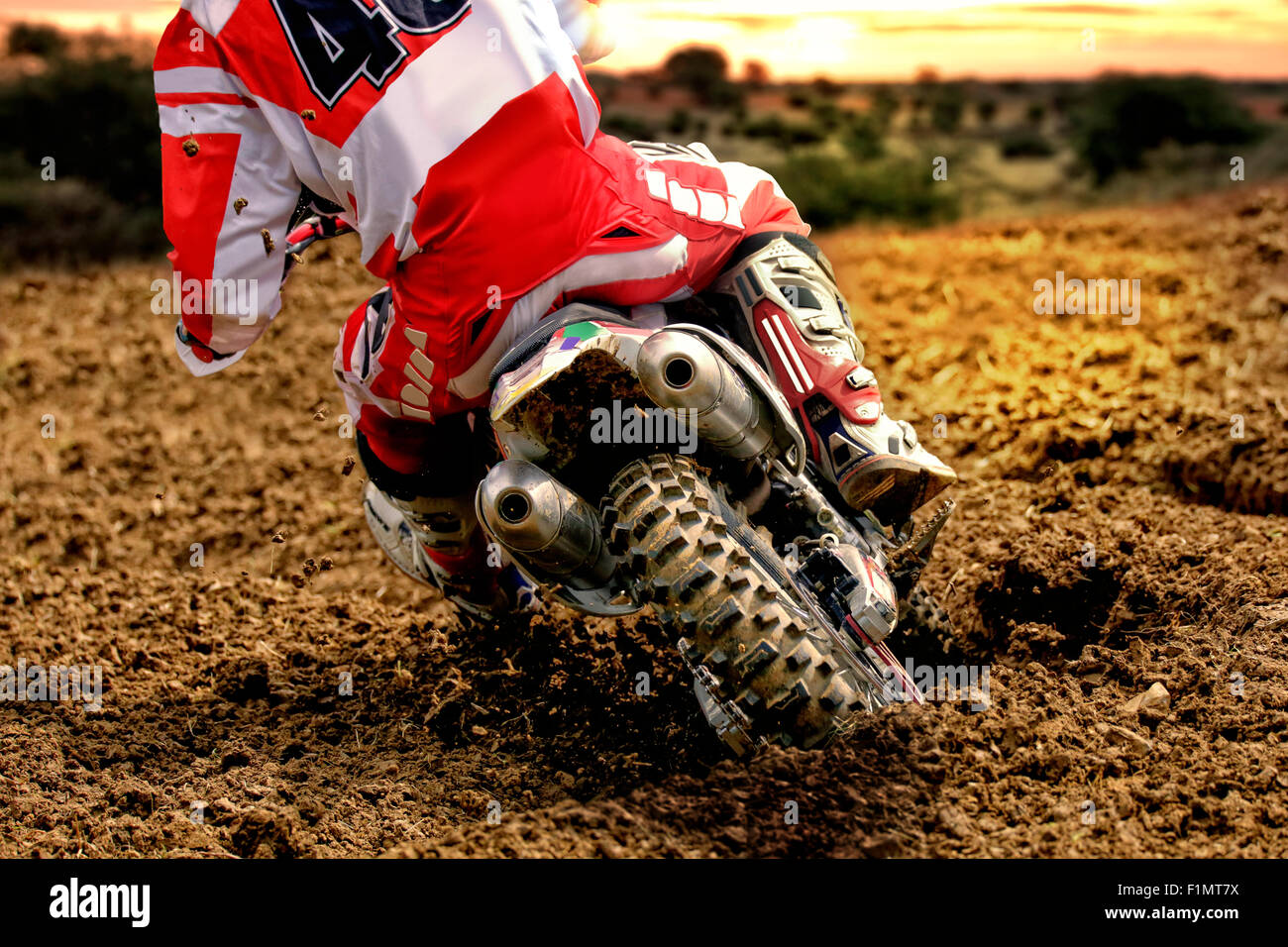 Vue arrière de la dérive motocross bike rider au coucher du soleil. L'arrière est de creuser profondément dans le sable et la saleté se jette dans l'air. Banque D'Images