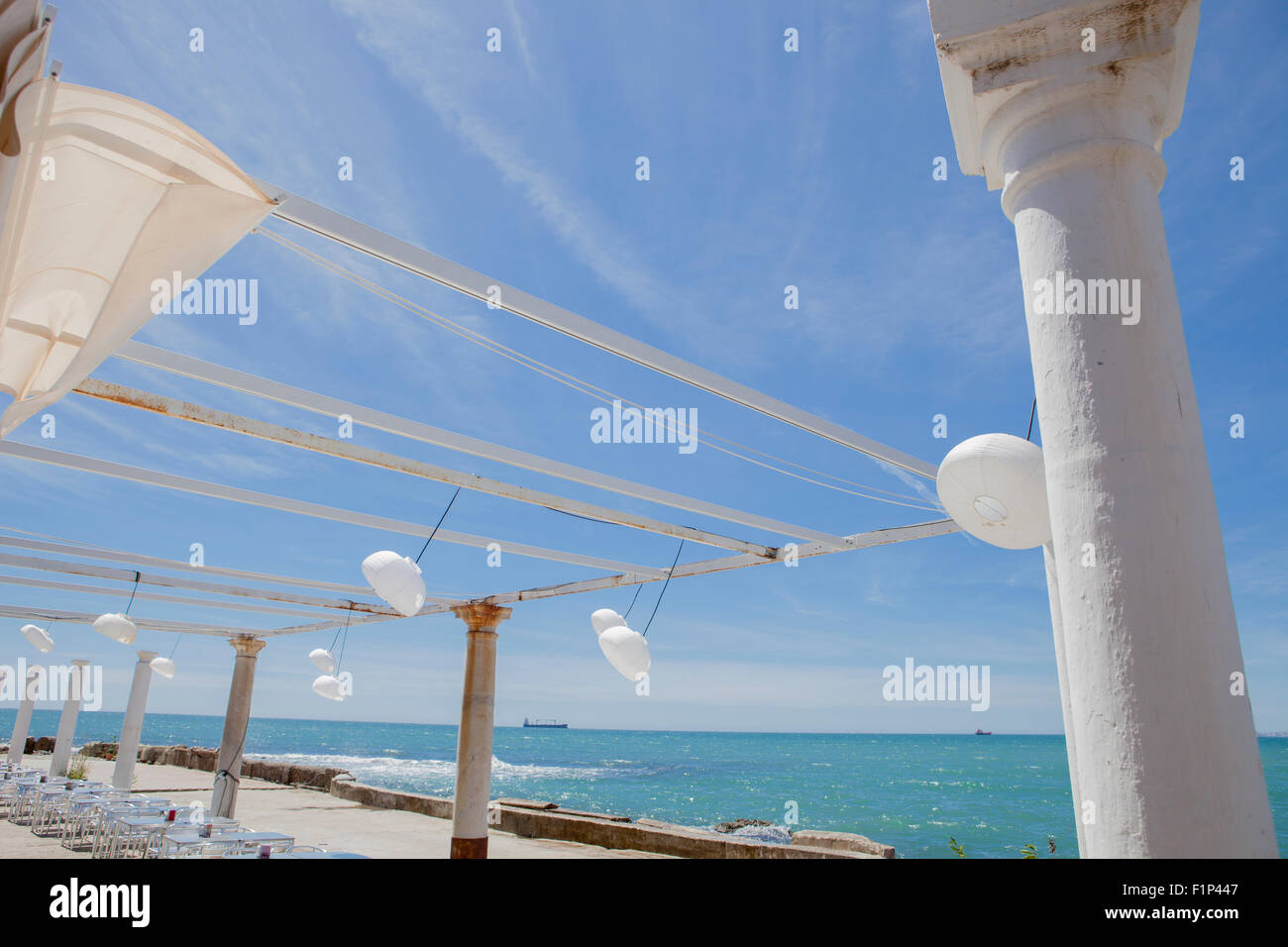 Terrasse au bord de la mer avec pergola, colonnes et lampes de papier un jour de vent Banque D'Images