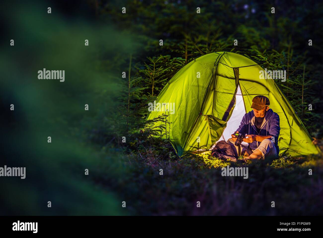 Camping de la forêt la nuit. L'âge moyen Caucasian Hiker avec son appareil photo numérique et de l'illuminé de nuit tente verte. La nuit Banque D'Images