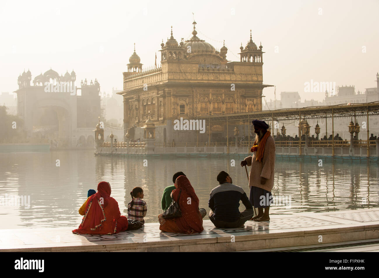 Amritsar, Punjab, en Inde. Le Temple d'Or - Harmandir Sahib - à l'aube avec un vieux message d'une famille Sikh assis en tailleur sur le côté du lac. Banque D'Images