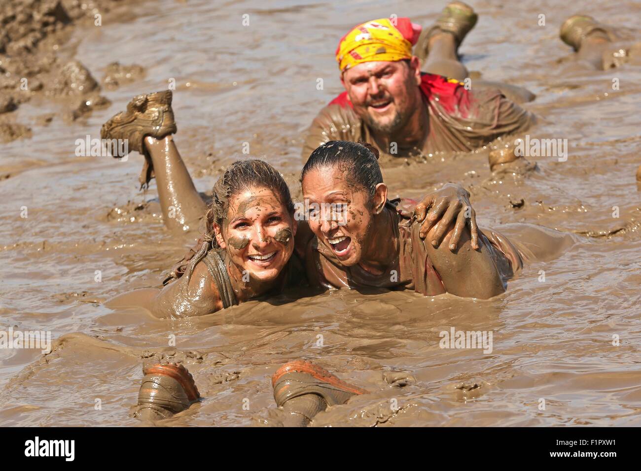 Deux femmes concurrents sourire alors qu'ils se traînent dans une piscine de boue pendant le général commandant's Cup Mud Run de Camp Pendleton, 12 juin 2015 à Oceanside, en Californie. La Mud Run est une course à travers la boue des fosses, des pentes glissantes et nageant à travers la boue épaisse à la ligne d'arrivée. Banque D'Images