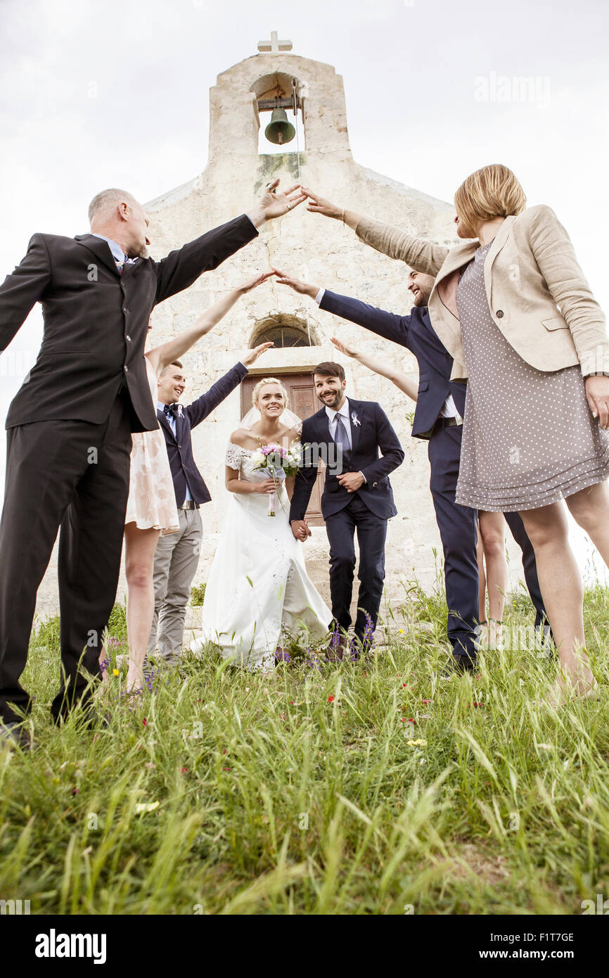Couple de jeunes mariés quitte chapelle entourée d'invités du mariage Banque D'Images