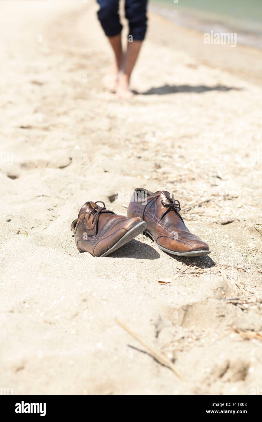 Chaussures placées dans le sable, homme qui marche en arrière-plan Banque D'Images