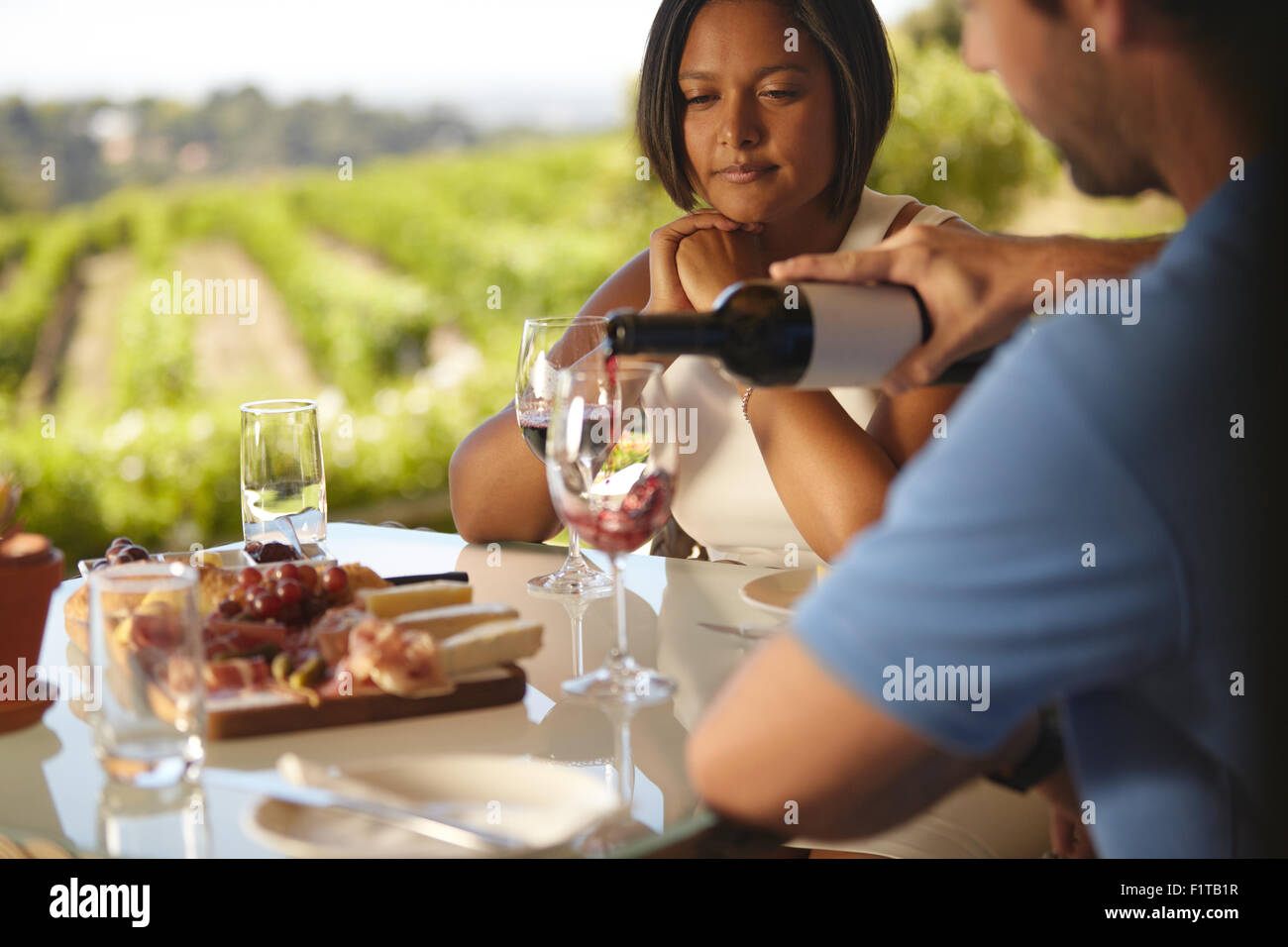 Jeune femme assise à une table tandis que l'homme verser un peu de vin rouge dans son verre. Au restaurant cave couple drinking red wine. Banque D'Images