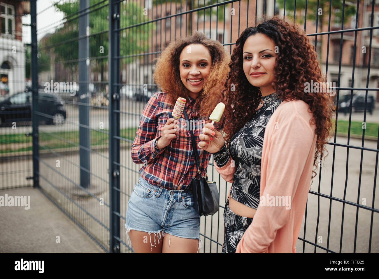 Portrait de belles jeunes femmes debout contre une clôture à la caméra à tout en mangeant de la crème glacée. Banque D'Images