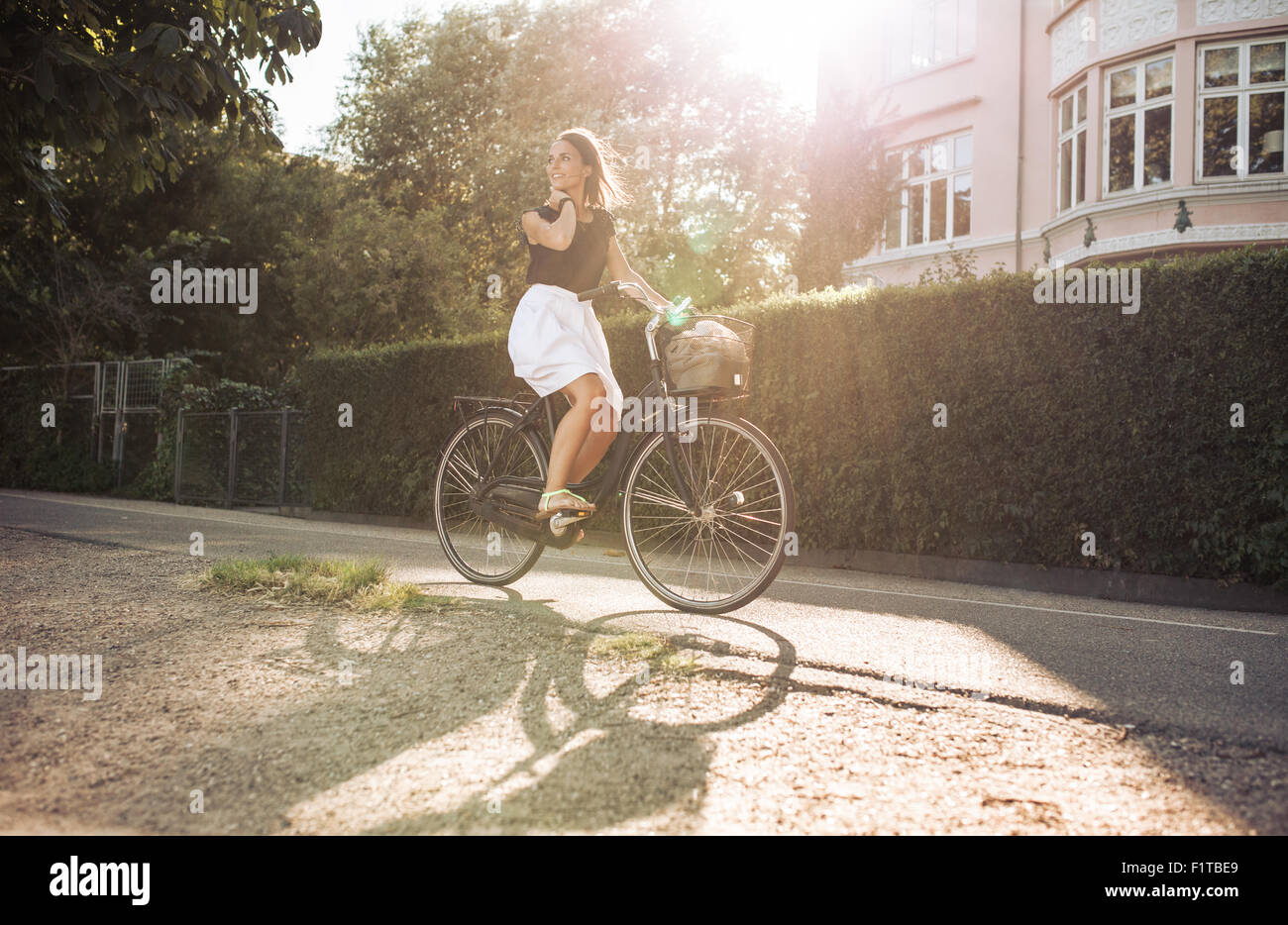 Pretty young woman enjoying balade à vélo à travers la rue. Femme à l'écart tout en souriant à vélo. Banque D'Images