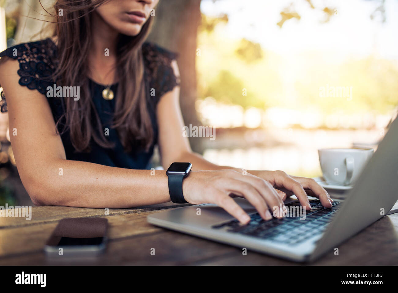 Jeune femme portant smartwatch en utilisant un ordinateur portable. Les femmes travaillant sur ordinateur portable dans un café en plein air. Banque D'Images Jeune femme portant smartwatch en utilisant un ordinateur portable. Les femmes travaillant sur ordinateur portable dans un café en plein air. Banque D'Images