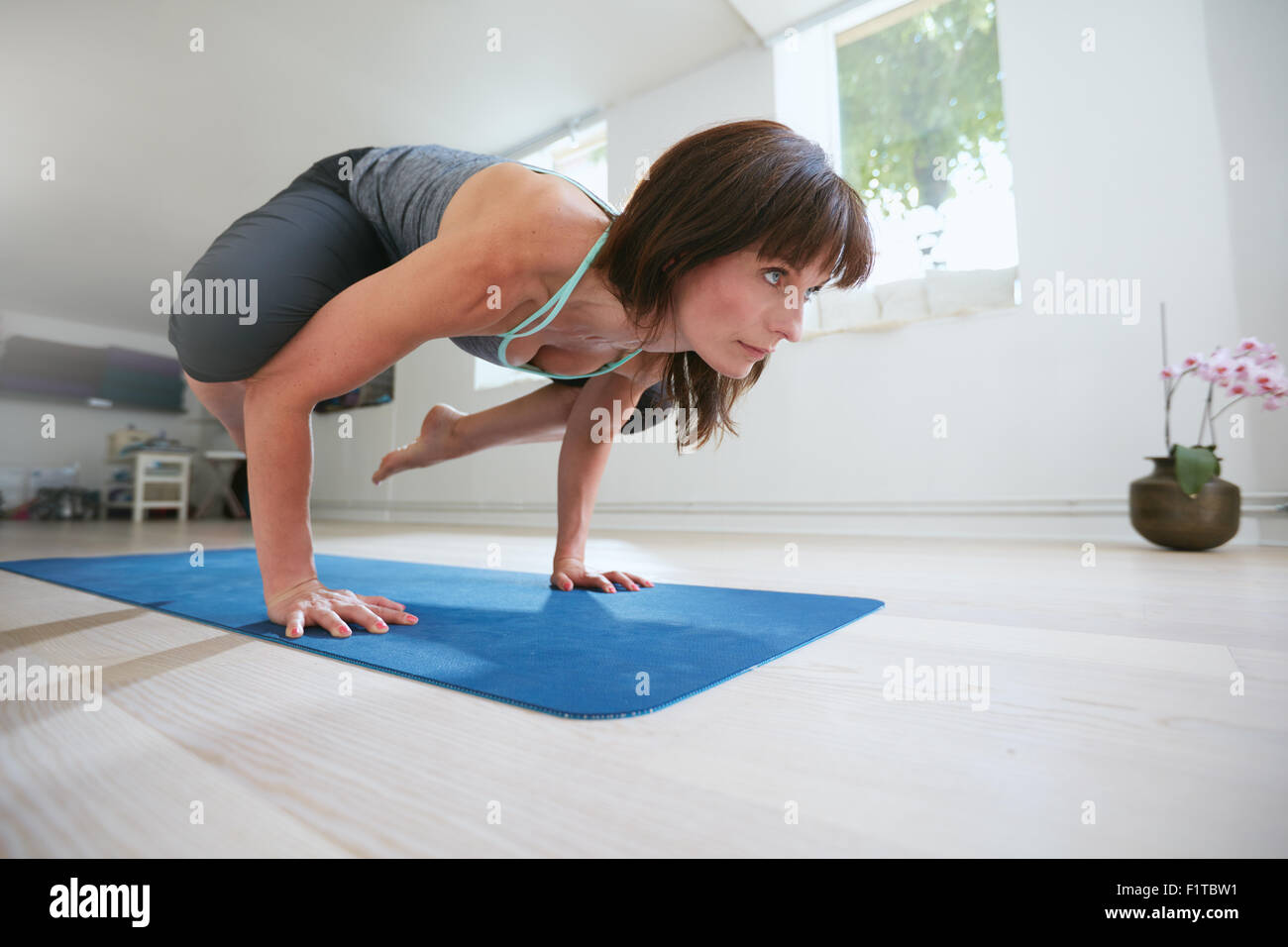 Remise en forme mature femme debout sur les mains, les pieds levés vers le haut de faire crane yoga pose - Bakasana. Femme debout sur les mains l'exercice Banque D'Images