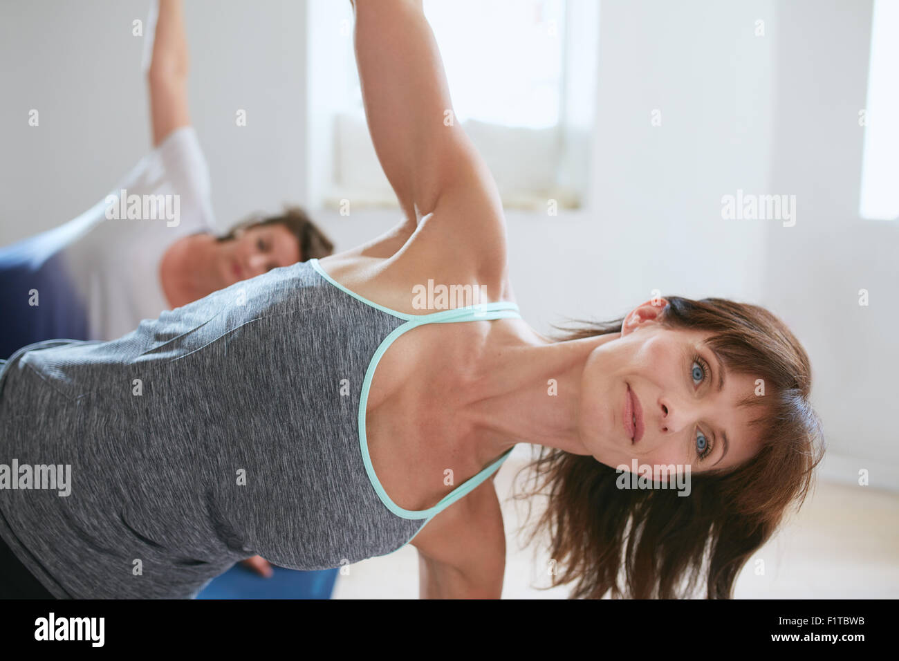 Portrait of mature woman s'étend dans une salle de sport. Fitness Trainer avec en arrière-plan étudiant faisant Ardha Chandrasana. demi-lune Banque D'Images