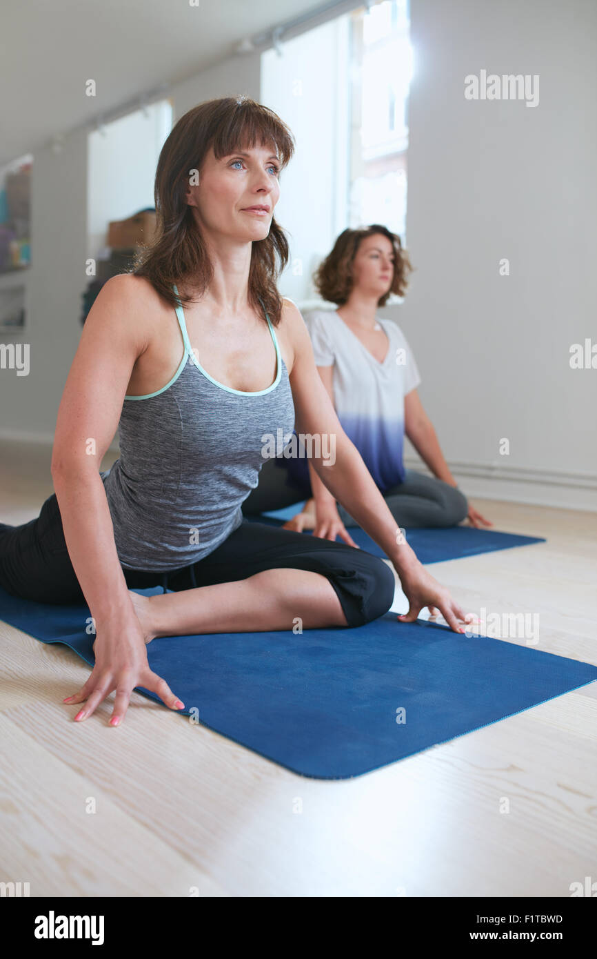 Remise en forme des femmes à l'instructeur de yoga dans pigeon poser sur son tapis de yoga en salle de sport. Les femmes au cours de la pratique de Kapotasaana. Banque D'Images