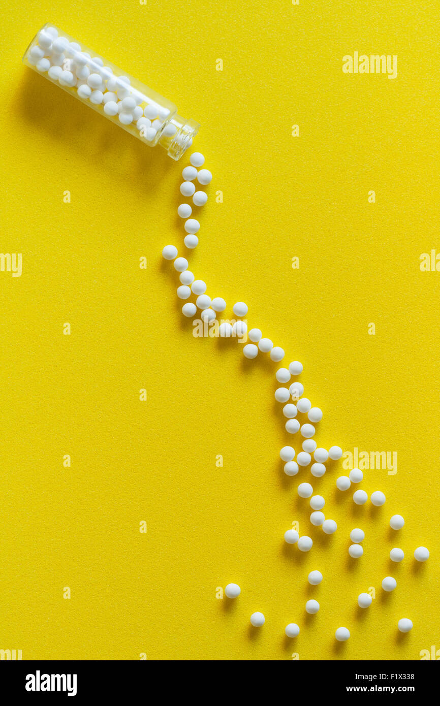Vue aérienne de pilules homéopathiques (fait à partir de la matière inerte - sucre/lactose) Effet de déversement à partir d'une bouteille sur la surface jaune. Banque D'Images