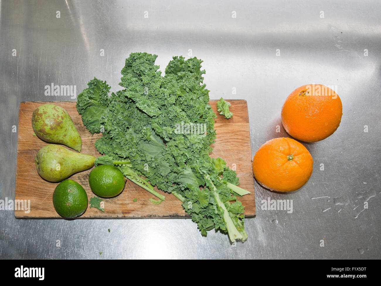 Le Kale, poires, fruits de la chaux et des oranges sur une planche à découper en bois dans l'évier de cuisine, les ingrédients pour un smoothie vert. Banque D'Images