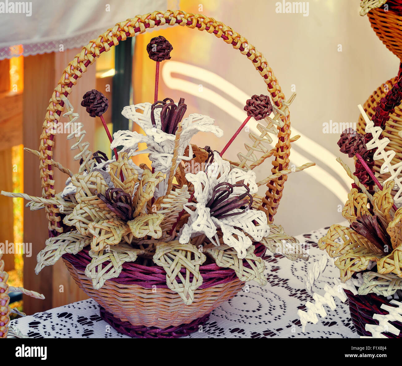 Paille tissée de belles fleurs dans un panier sur une table couverte d'une nappe en dentelle. Ce produits à vendre à la foire. Banque D'Images