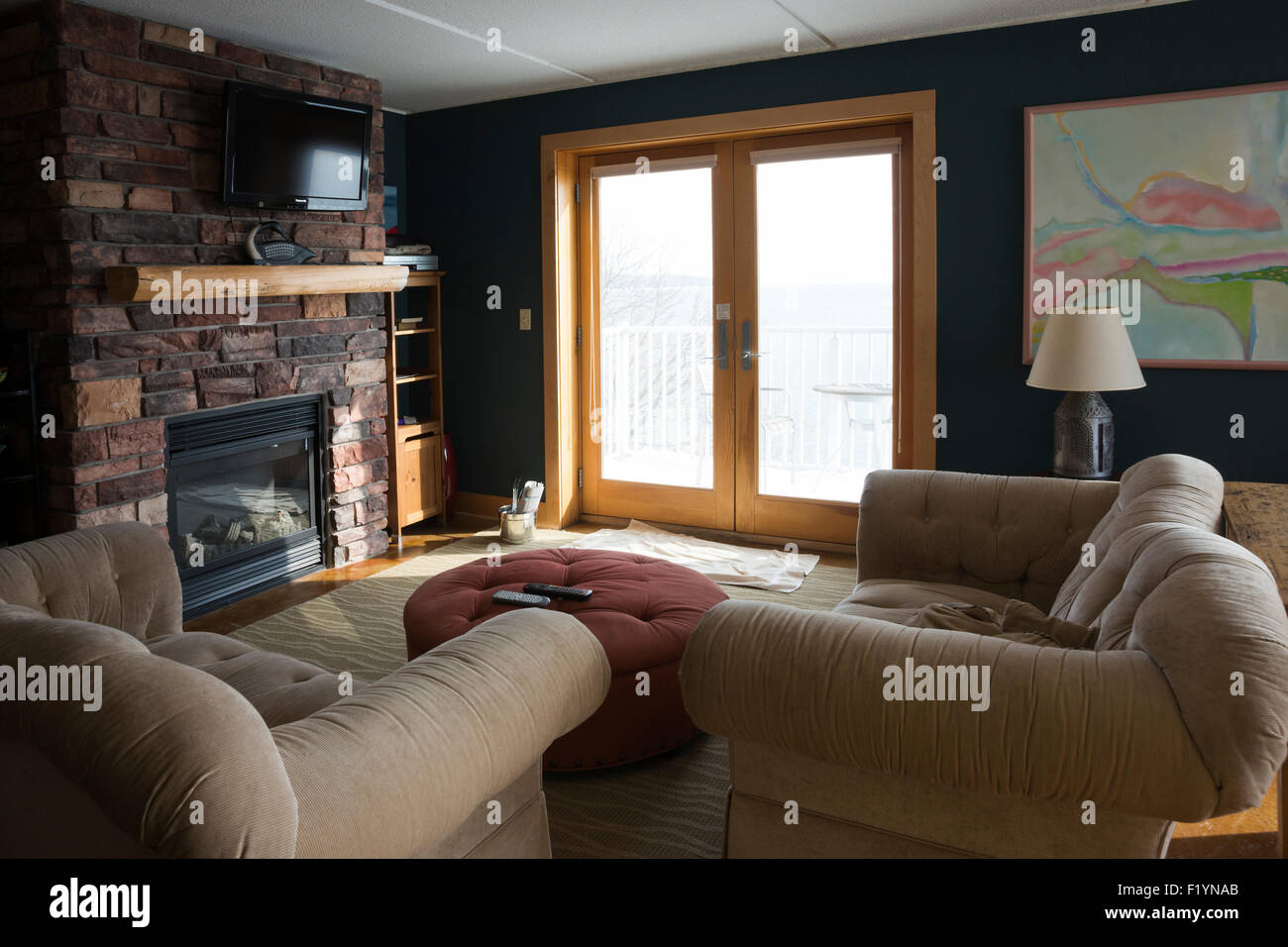 Hôtel suite avec fauteuils chaises beige et ottomane face à une cheminée en briques et des portes françaises donnant sur le lac Supérieur Banque D'Images