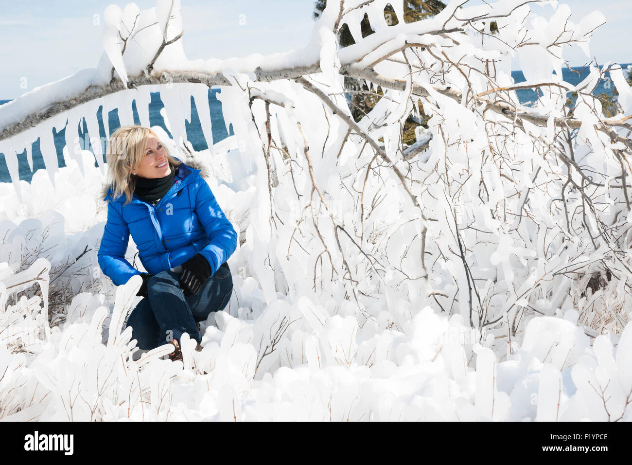 Une femme blonde est assise sous un couvert de glace dans une direction générale de la forêt gelée le long du lac Supérieur dans l'hiver, après une vague de 15 pieds s'est écrasé je Banque D'Images
