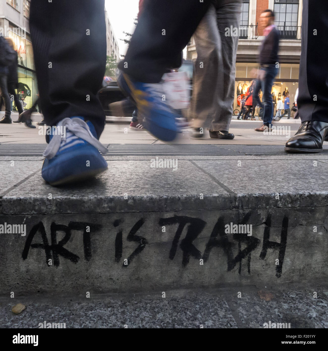 Londres, Angleterre. Bordure de rue avec "l'Art est Trash' graffiti, avec pieds, en bleu les formateurs et cuir poli. Banque D'Images