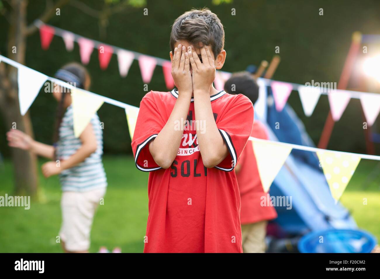 Garçon couvrant ses yeux pour cache-cache avec soeur et son frère dans le jardin Banque D'Images
