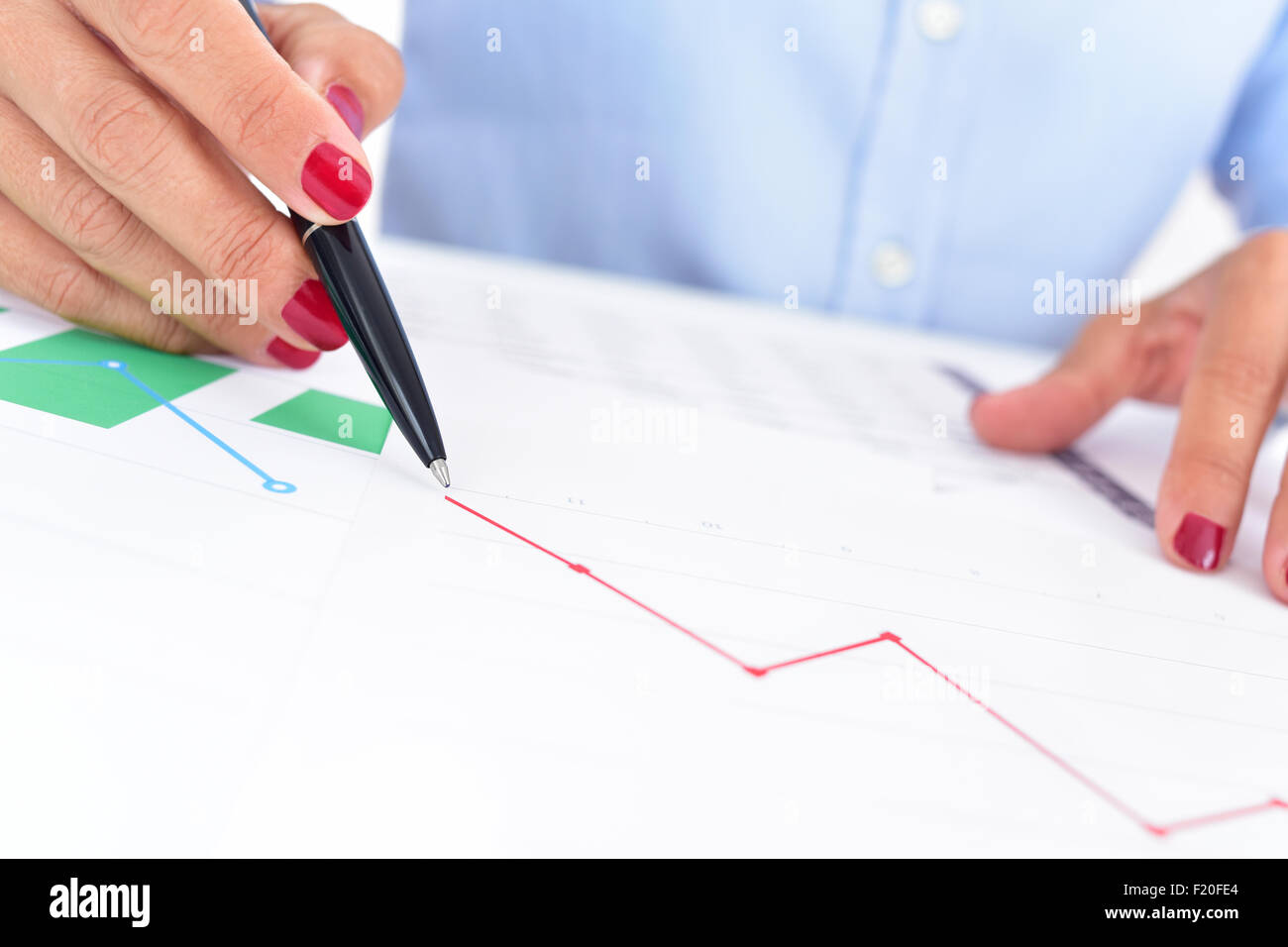 Libre d'une femme à son bureau bureau plein de graphiques et tableaux, observe un graphique avec une tendance à la baisse Banque D'Images