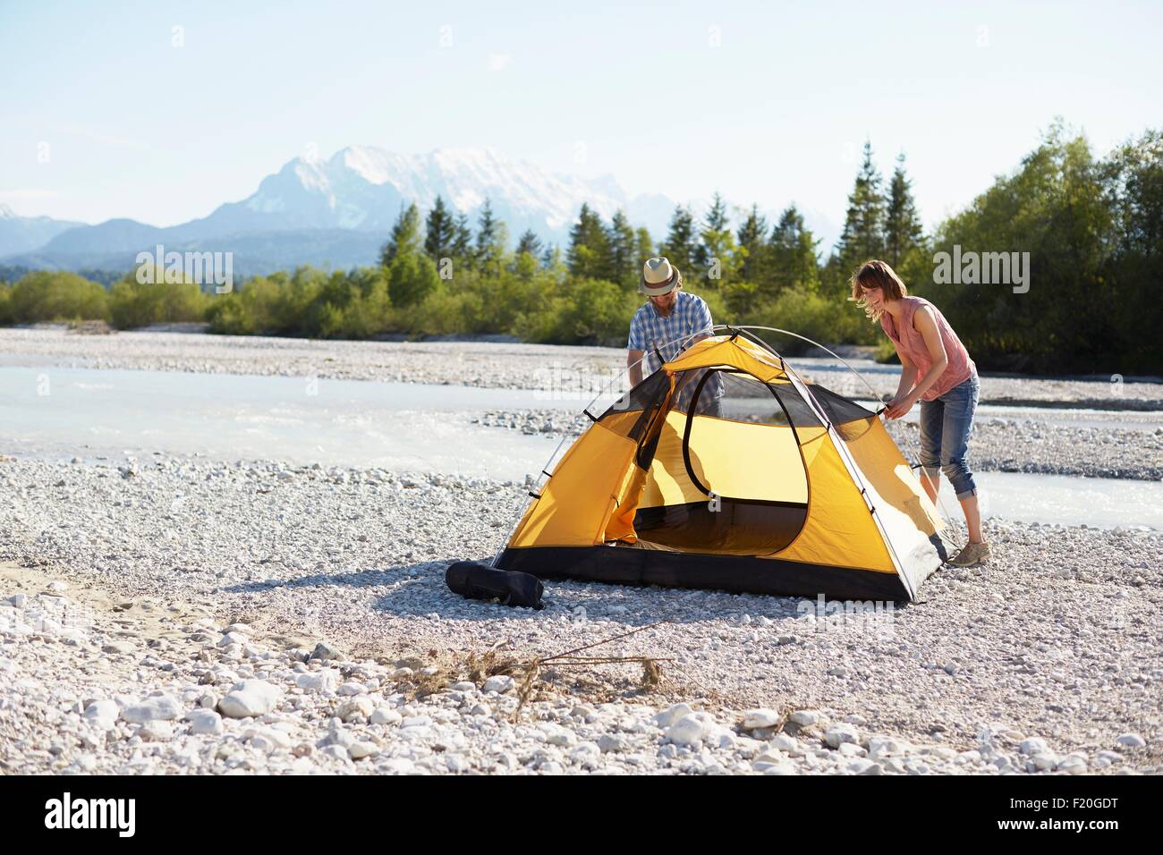 Couple érigeant tente jaune près de l'eau, Wallgau, Bavière, Allemagne Banque D'Images