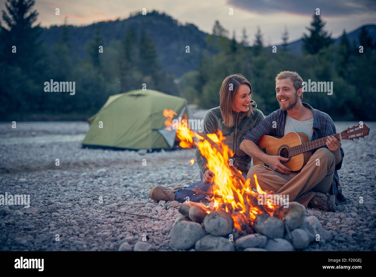 Jeune couple assis par camp à jouer de la guitare Banque D'Images