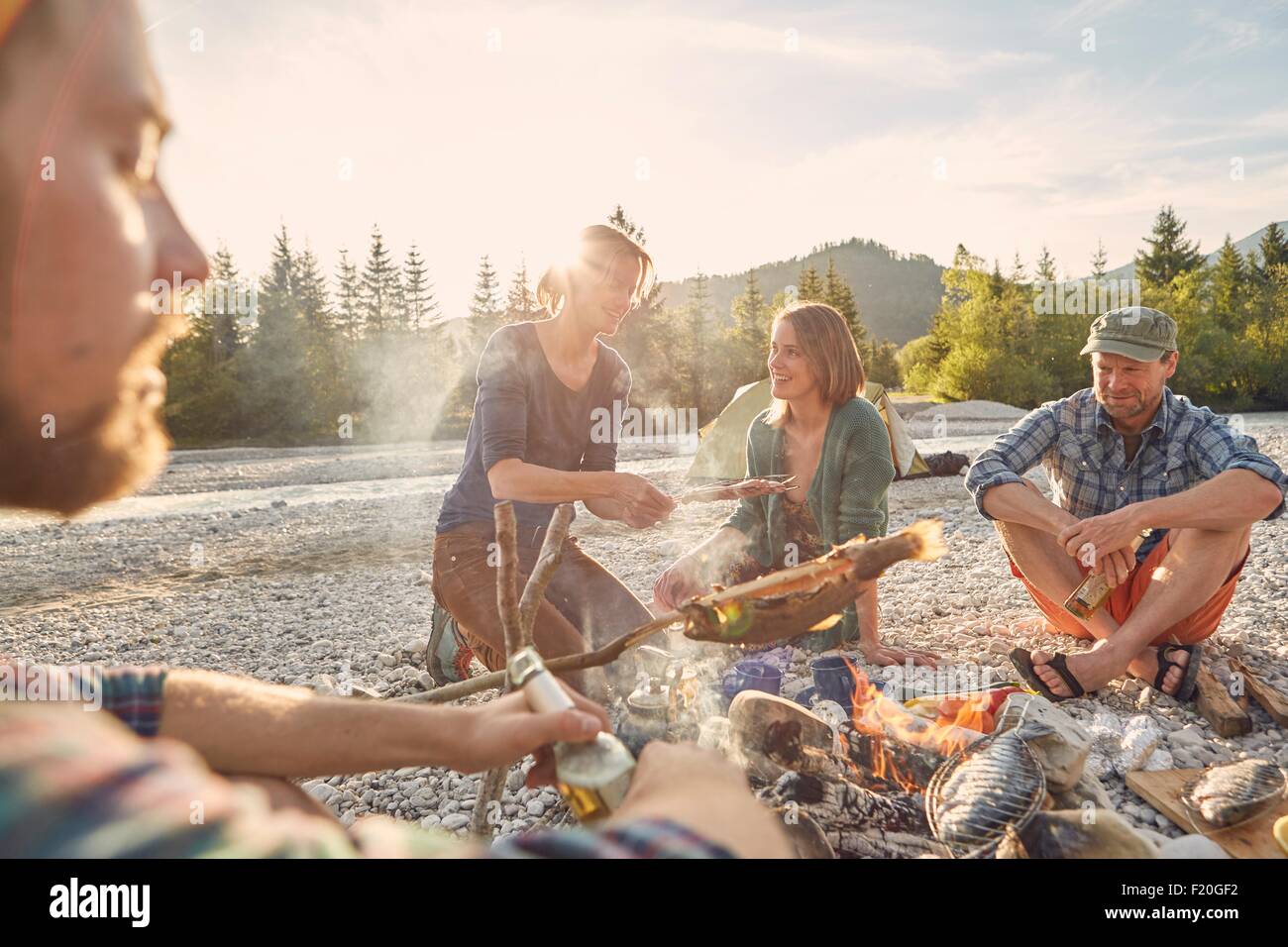 Les adultes assis autour de camp Cuisiner les poissons Banque D'Images
