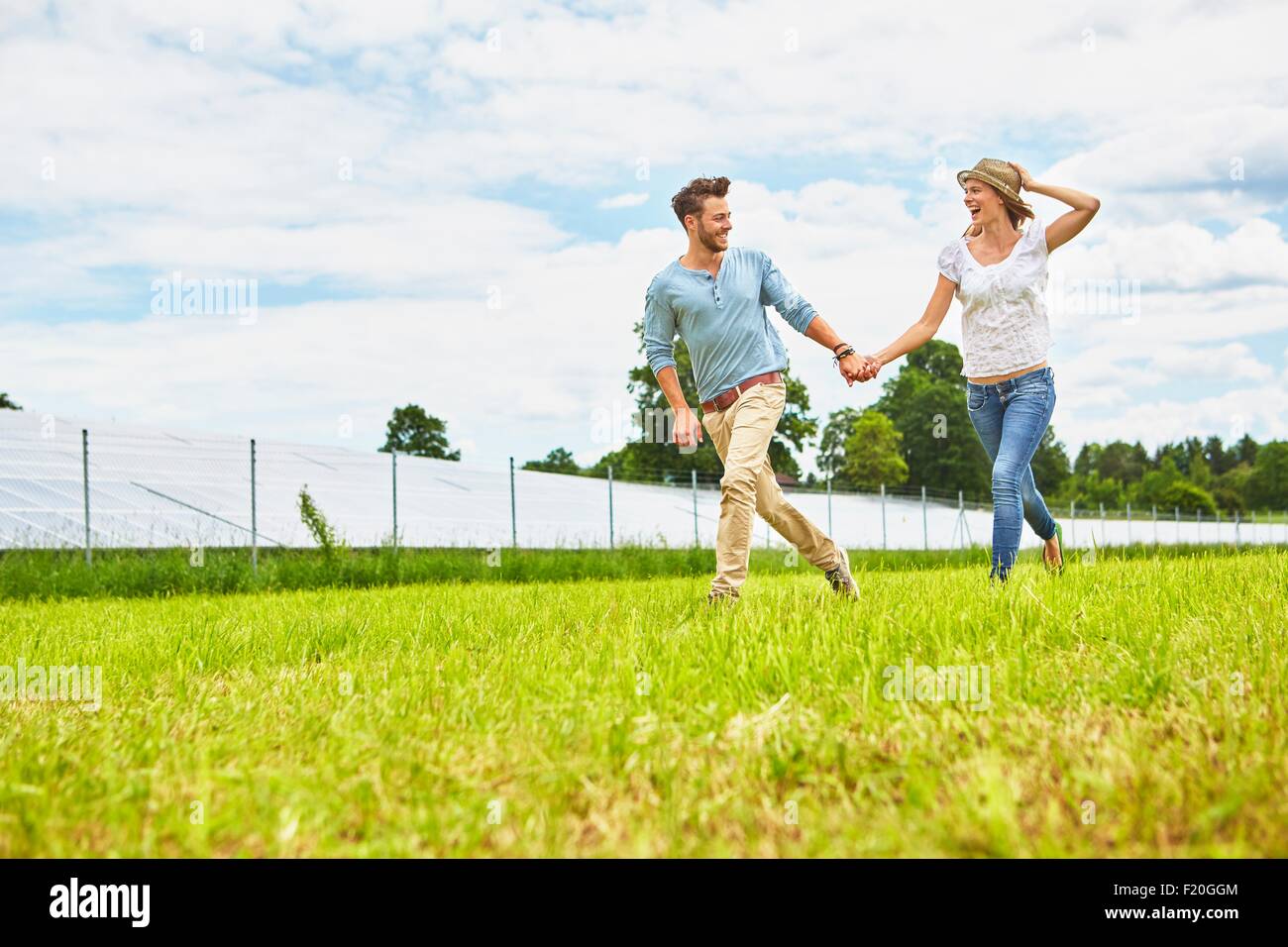 Young couple holding hands, courant à travers champs, à côté de la ferme solaire Banque D'Images