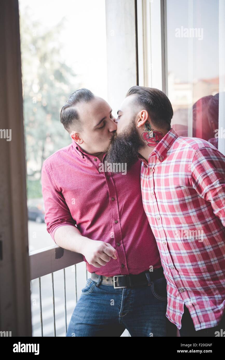 Gay couple kissing by window Banque D'Images