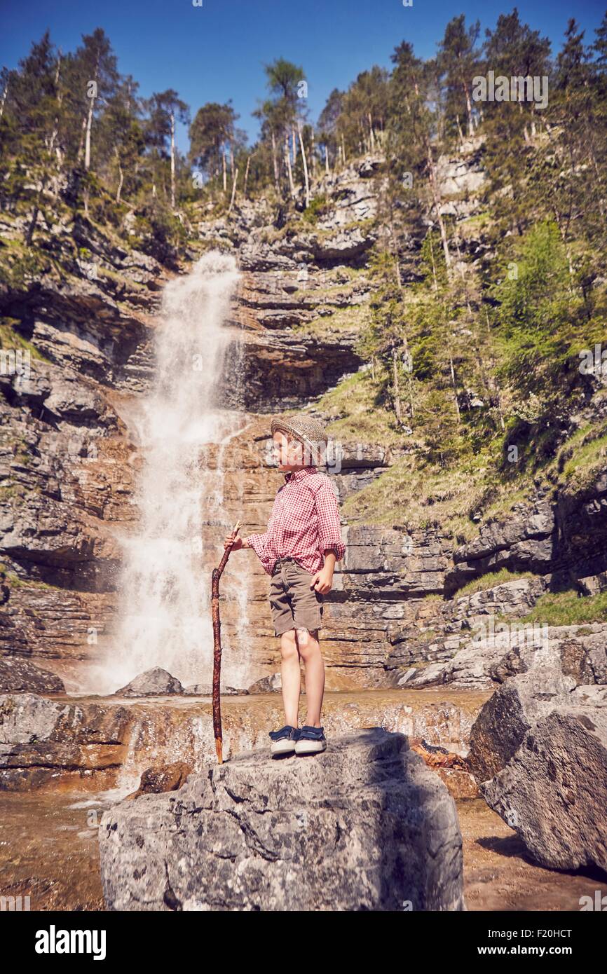 Jeune garçon, debout sur la roche à côté d'une cascade, holding stick Banque D'Images