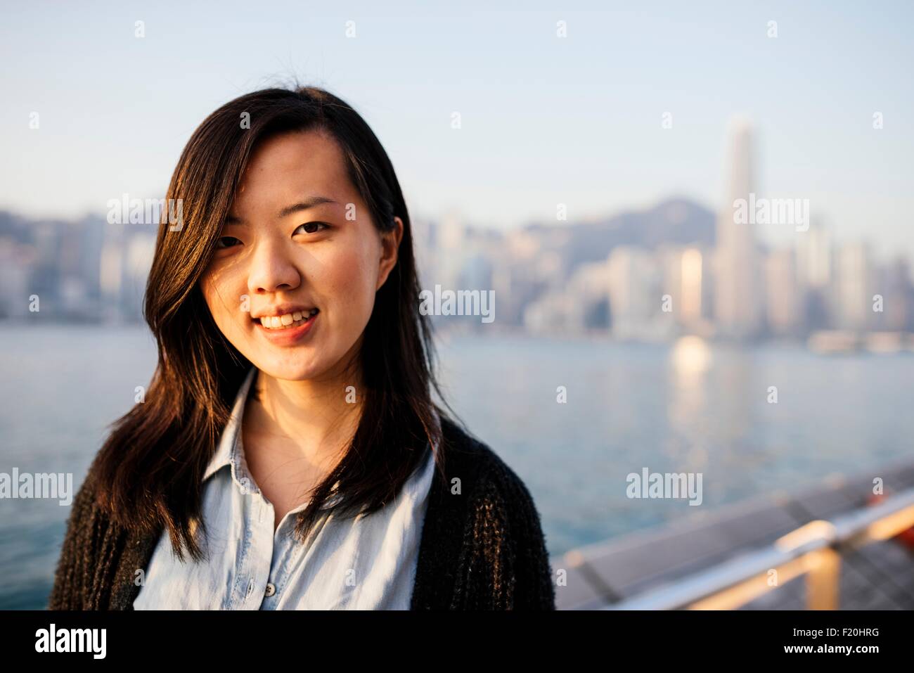 Portrait de jeune femme aux cheveux longs portant chemise et veste en face de l'eau, looking at camera Banque D'Images
